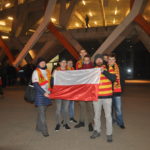 2 nauczycieli z uczniami przed stadionem z flagą Polski