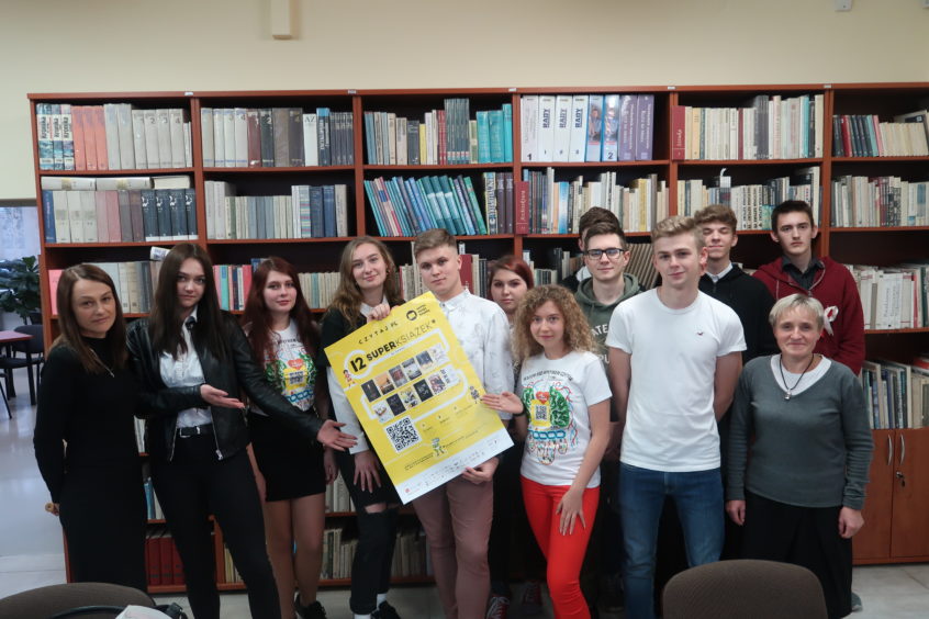 Uczniowie z plakatem akcji z nauczycielkami w bibliotece