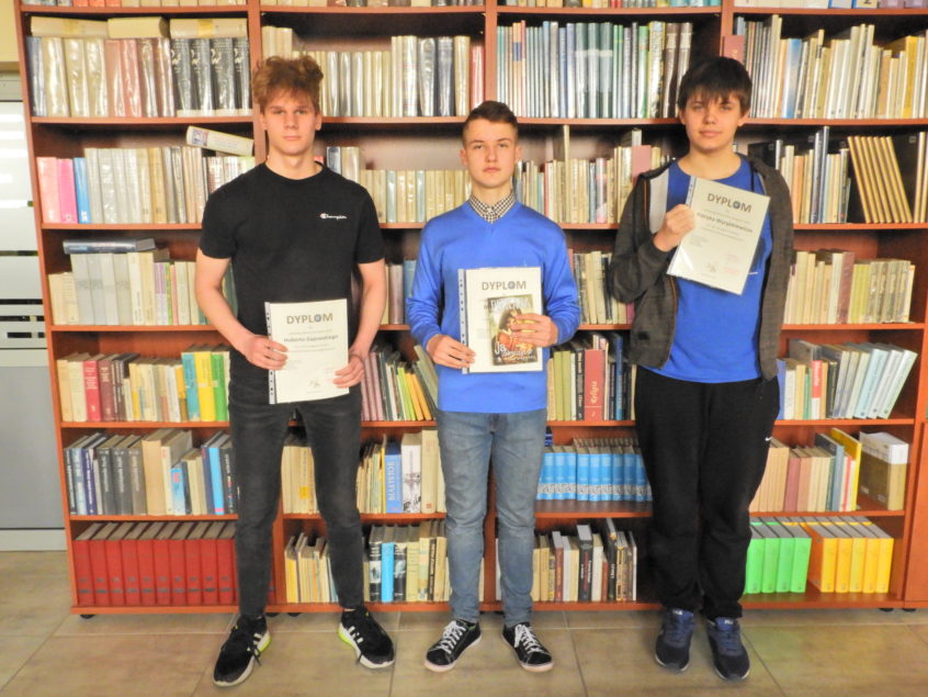 Zwycięzcy konkursu z dyplomami na tle regałów bibliotecznych