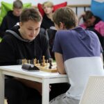 Uczniowie rozgrywający partię szachów, w tle uczniowie na pufach