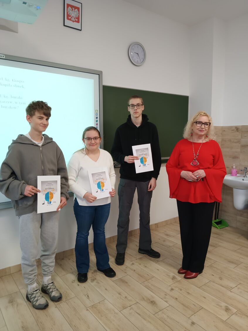 3 uczestników z dyplomami i Panią Dyrektor Anną Niczyporuk stoi w sali matematycznej